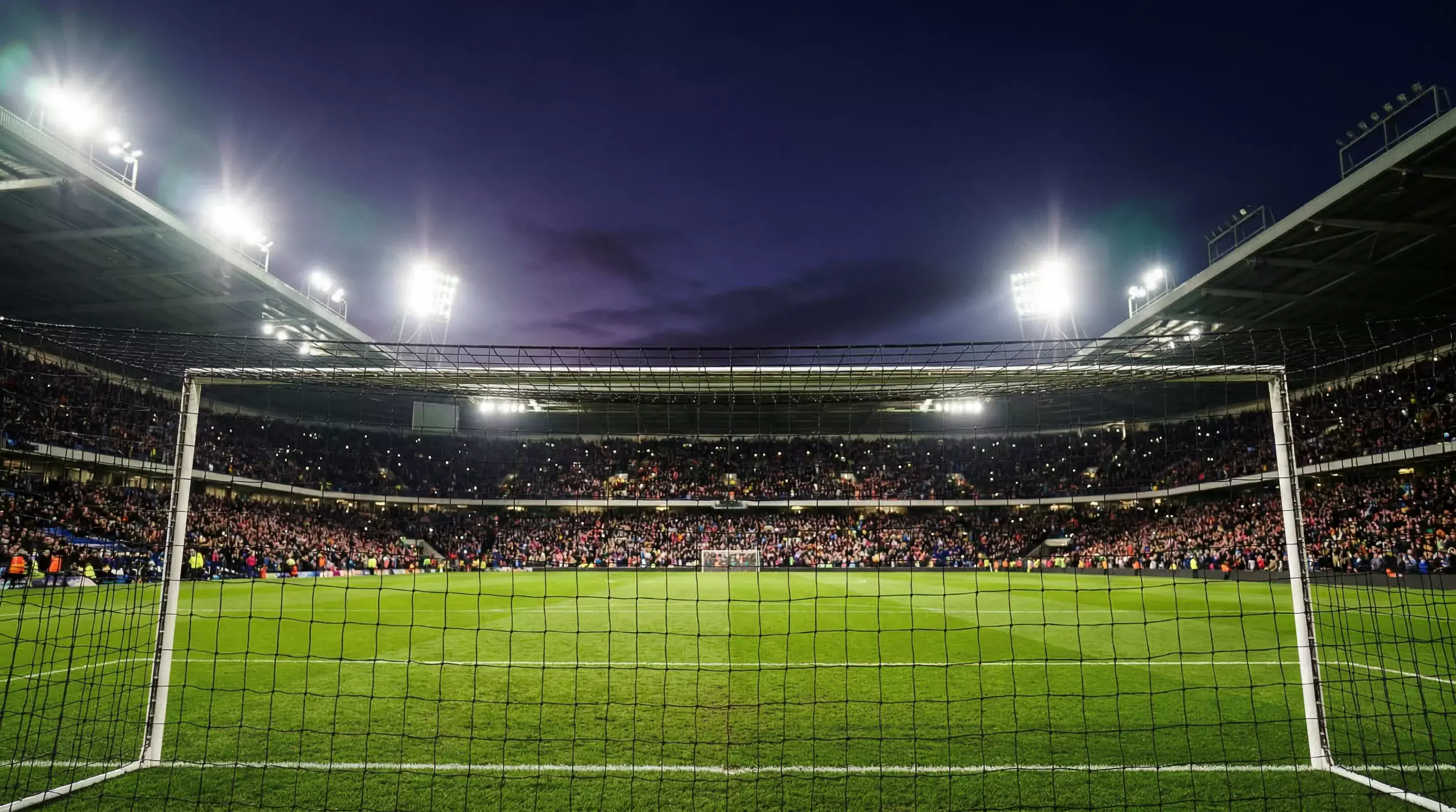 Estadio de la Premier League iluminado durante un partido nocturno con afición en las gradas